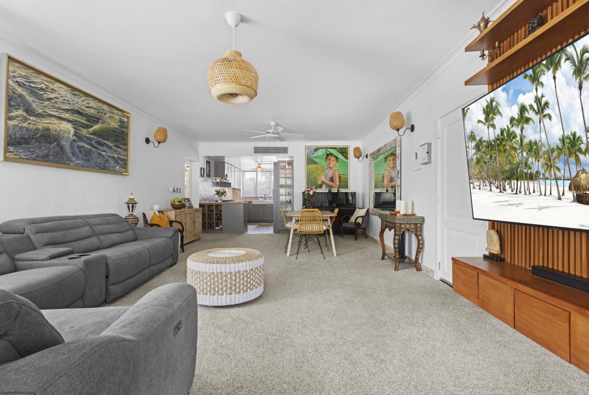 buyDRproperty Bright living room with a gray sofa, dining area, and beach scene on TV. Sosua Real Estate