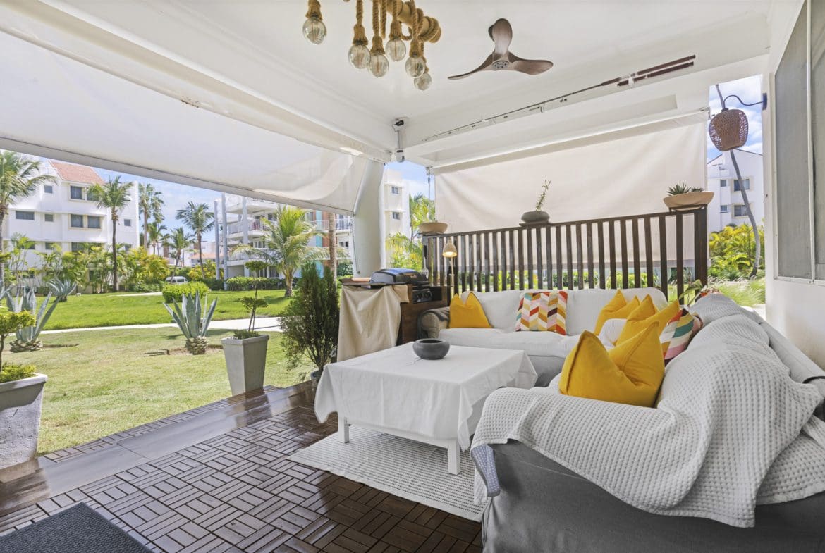 buyDRproperty Covered outdoor patio with white sofa, colorful pillows, and garden view. Sosua Real Estate