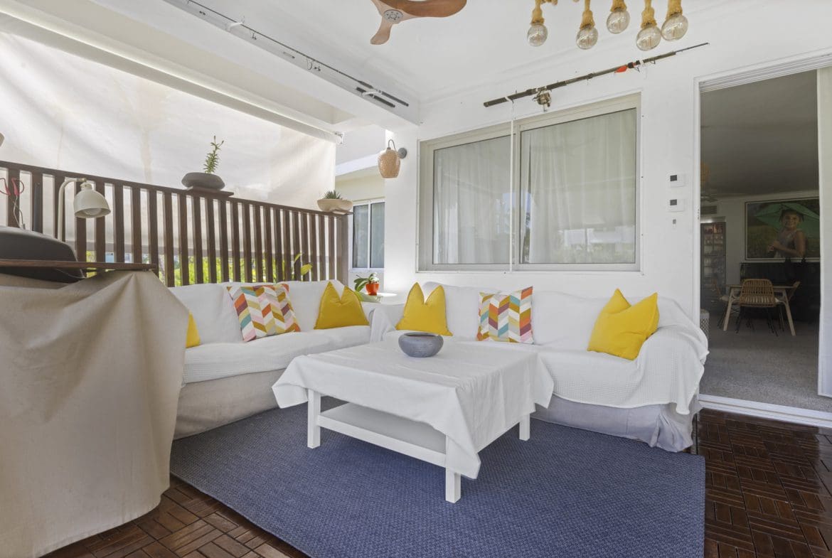 buyDRproperty Cozy outdoor living space with white sofa, blue rug, and fishing rods above window. Sosua Real Estate