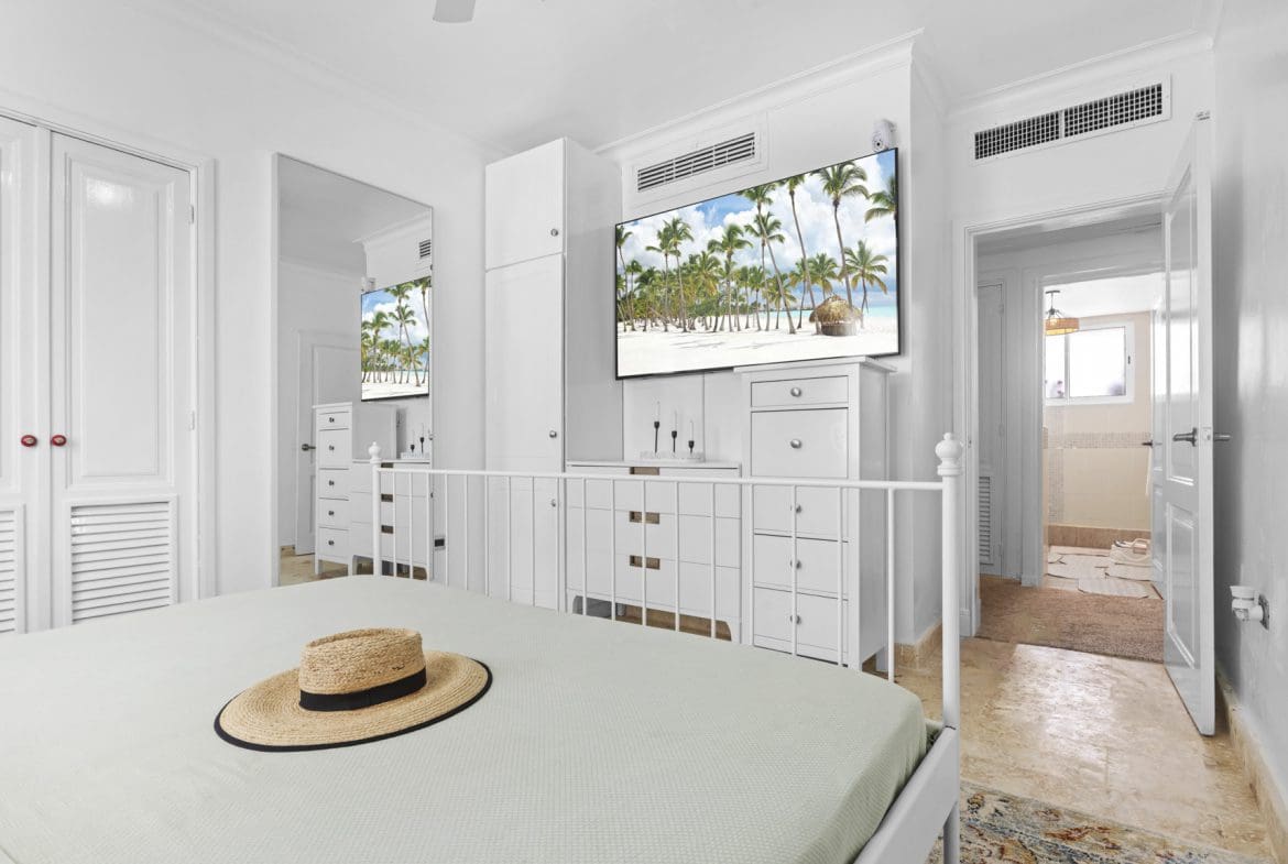 buyDRproperty Bright bedroom with beach scene on TV, hat on bed. Sosua Real Estate