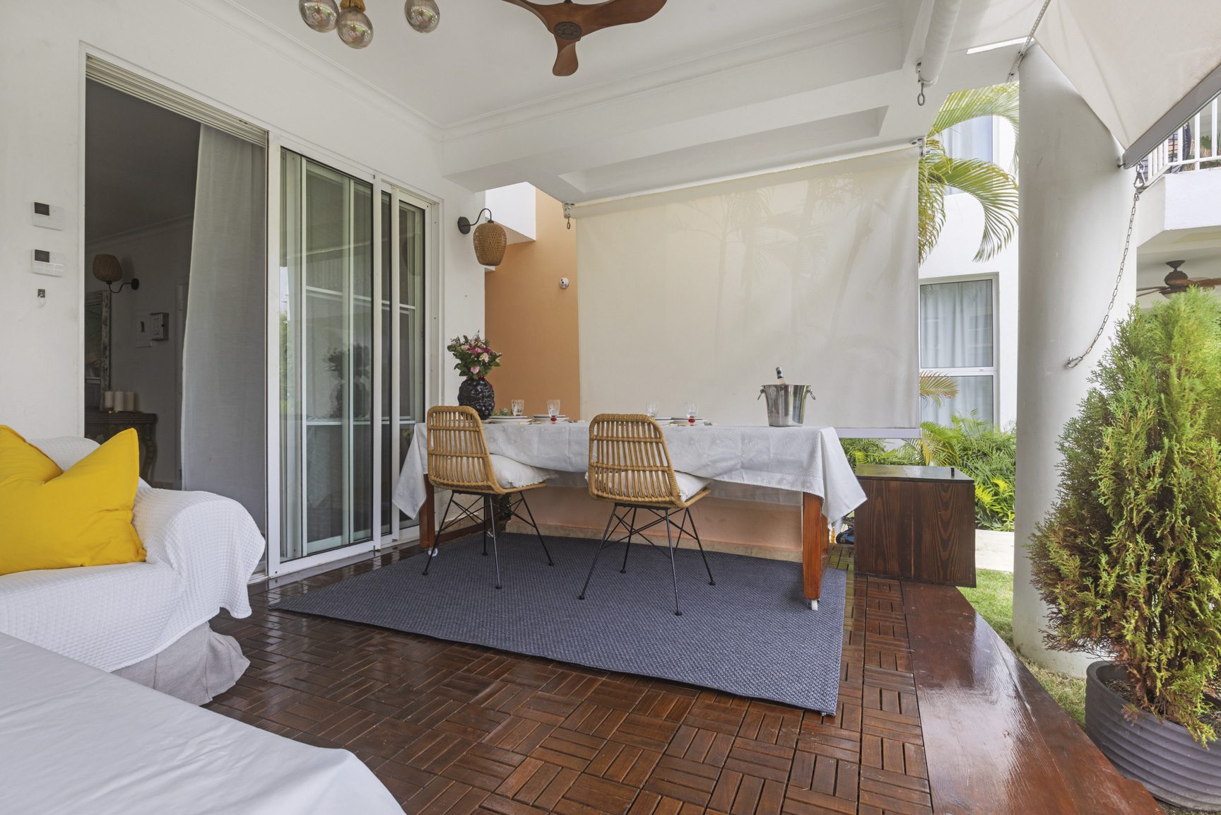 buyDRproperty Outdoor dining area with table set for a meal on a wooden patio, featuring a white sofa and lush greenery. Sosua Real Estate