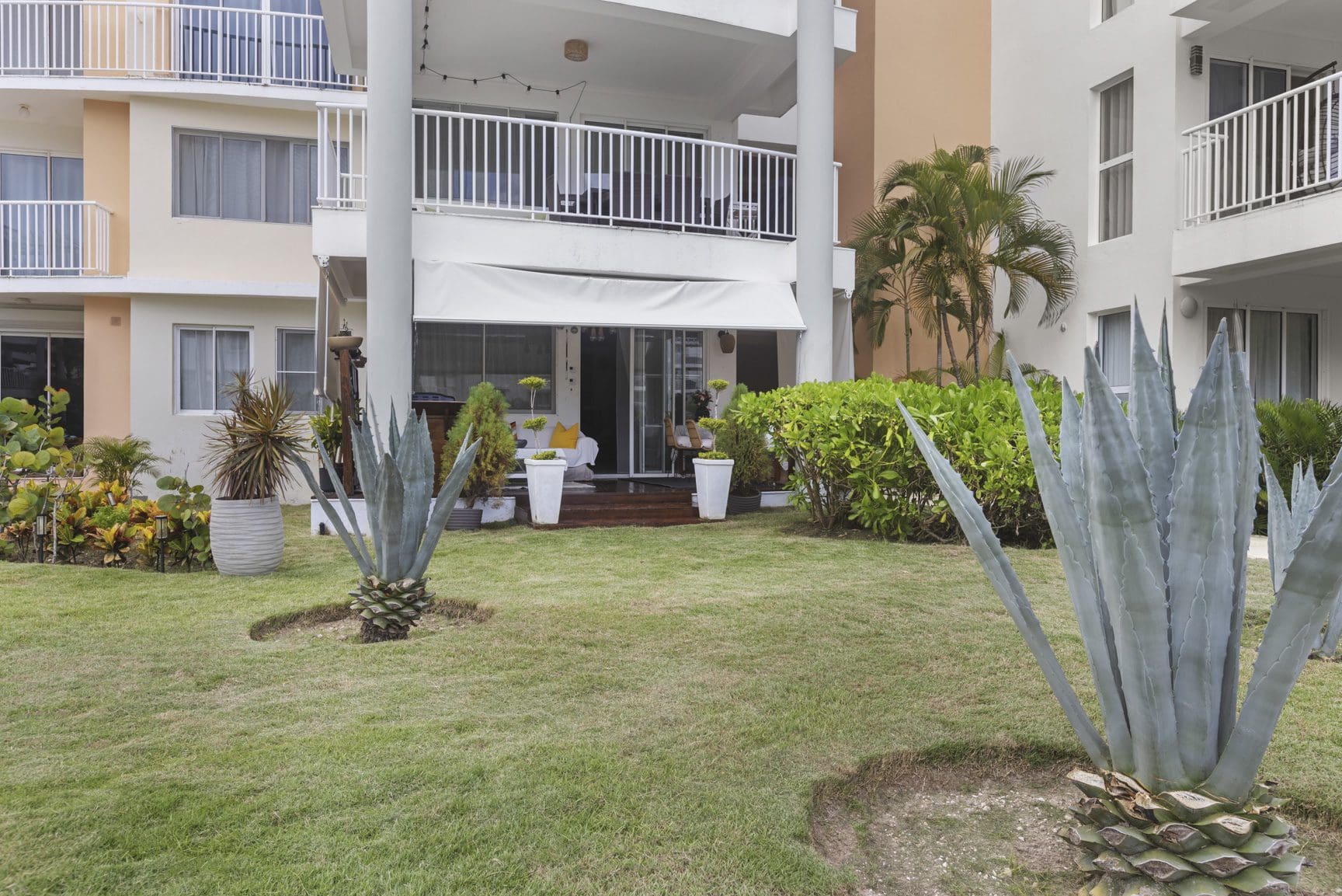 buyDRproperty Lush lawn with agave plants outside a modern condo building with white awnings and balconies. Sosua Real Estate