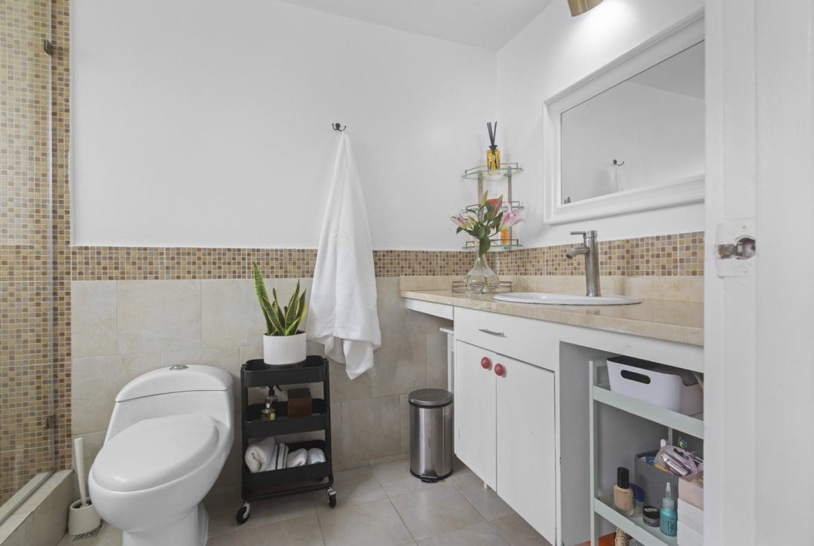 buyDRproperty Modern bathroom with white tiles, white toilet, countertop with sink, mirror, and shelving Sosua Real Estate