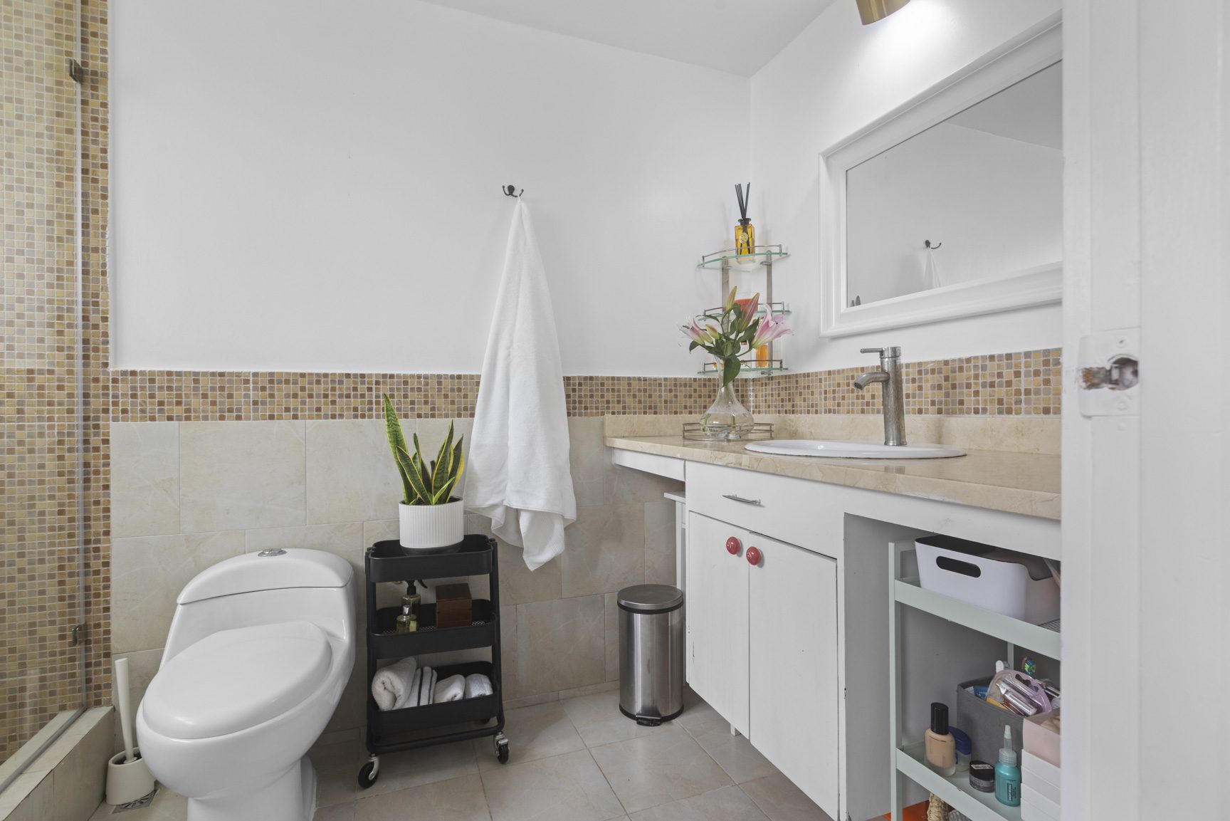 buyDRproperty Modern bathroom with white tiles, white toilet, countertop with sink, mirror, and shelving Sosua Real Estate