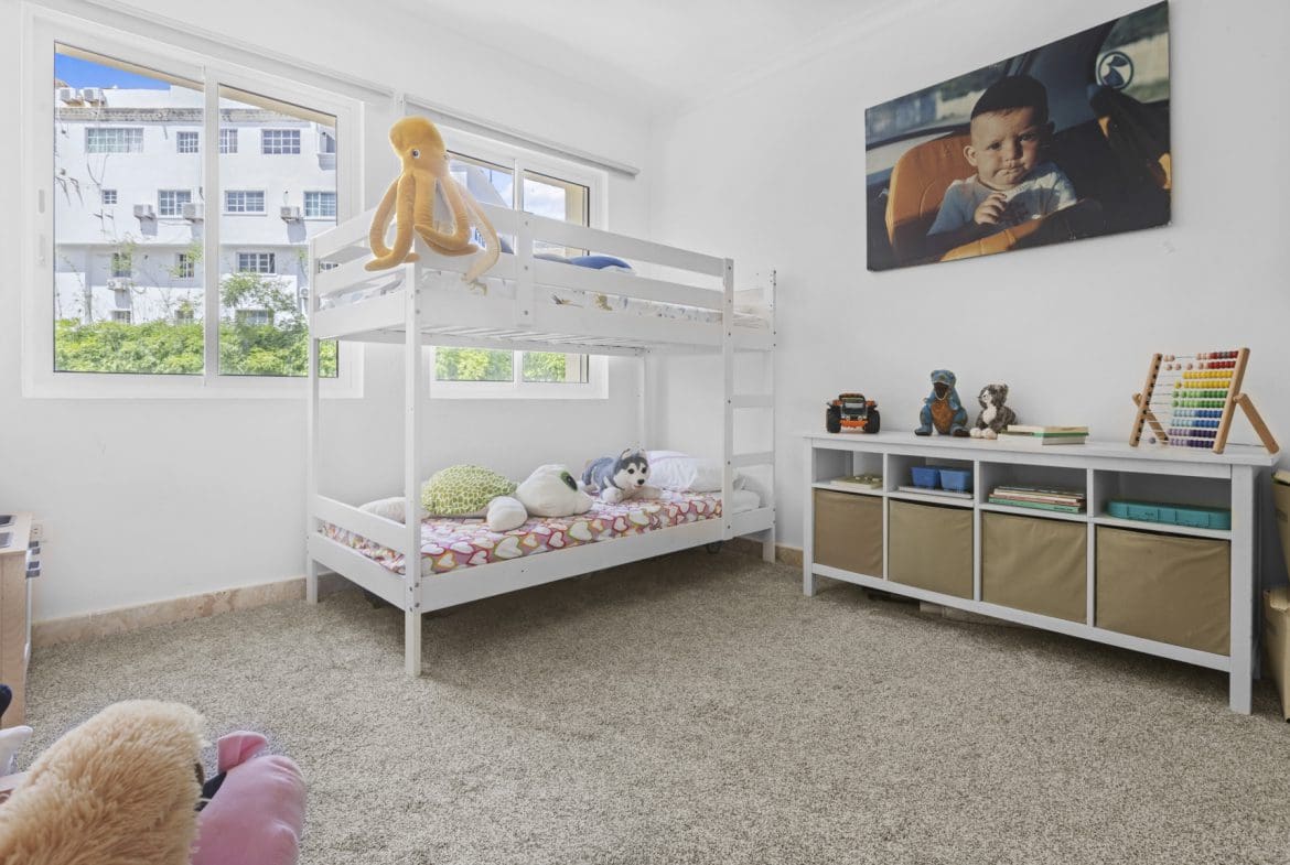 buyDRproperty Bright children's room with white bunk beds, soft toys, and a baby portrait on the wall. Sosua Real Estate
