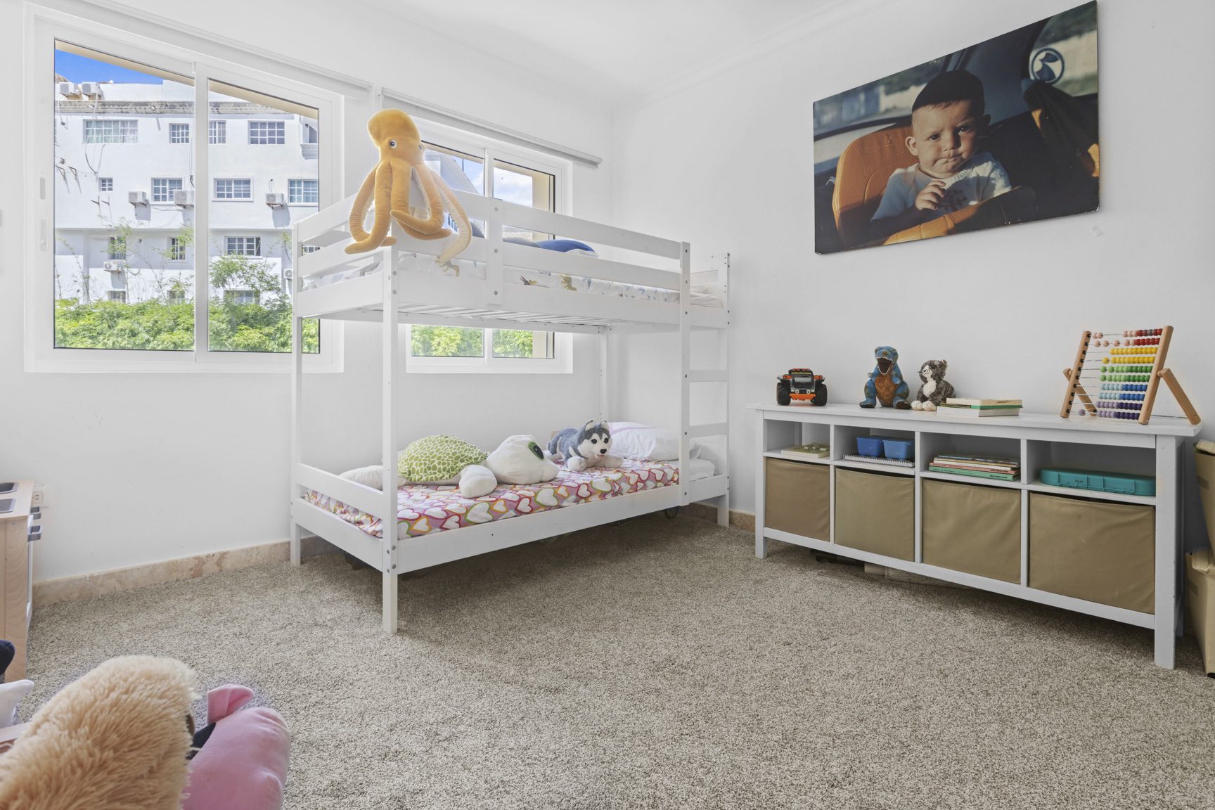 buyDRproperty Bright children's room with white bunk beds, soft toys, and a baby portrait on the wall. Sosua Real Estate