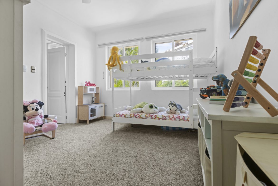 buyDRproperty Bright kids' room with white bunk beds, toys, and a play kitchen, creating a cheerful and playful atmosphere. Sosua Real Estate