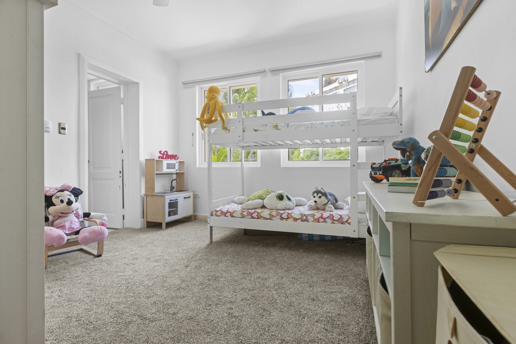 buyDRproperty Bright kids' room with white bunk beds, toys, and a play kitchen, creating a cheerful and playful atmosphere. Sosua Real Estate