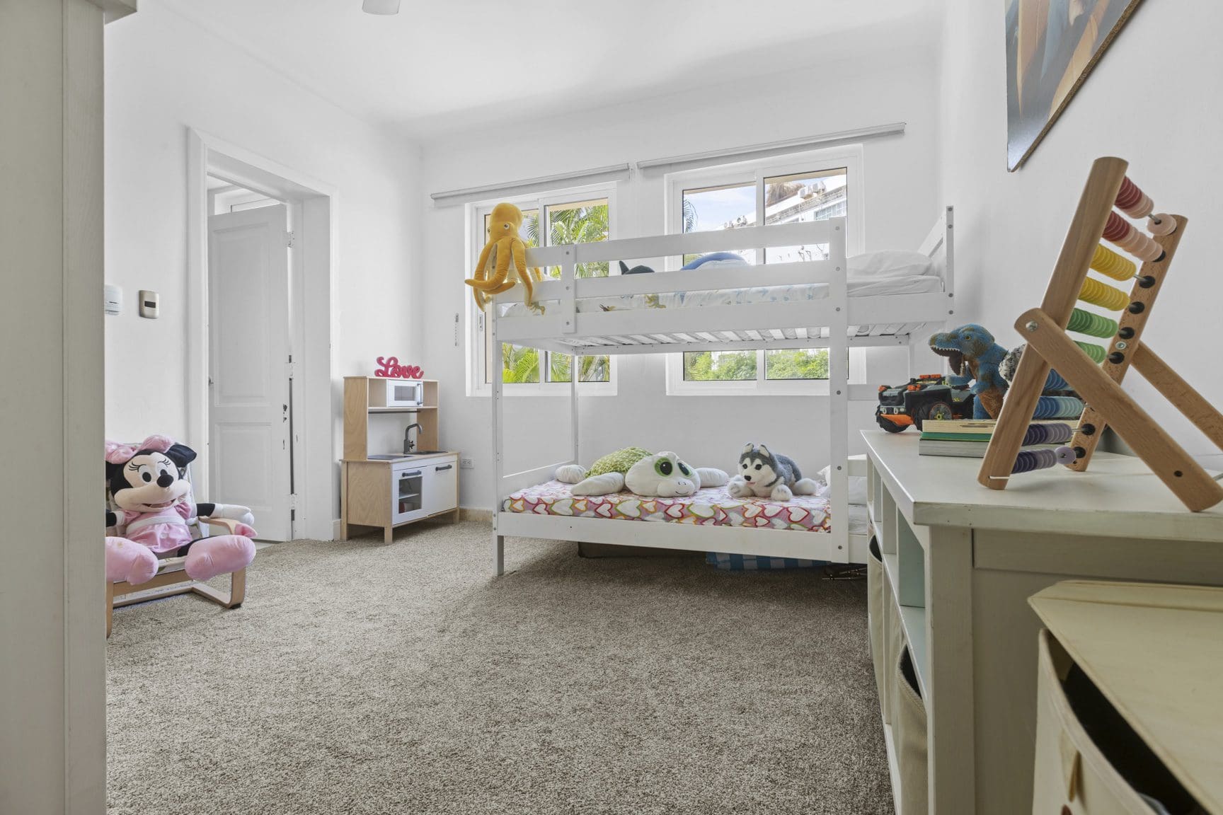 buyDRproperty Bright kids' room with white bunk beds, toys, and a play kitchen, creating a cheerful and playful atmosphere. Sosua Real Estate