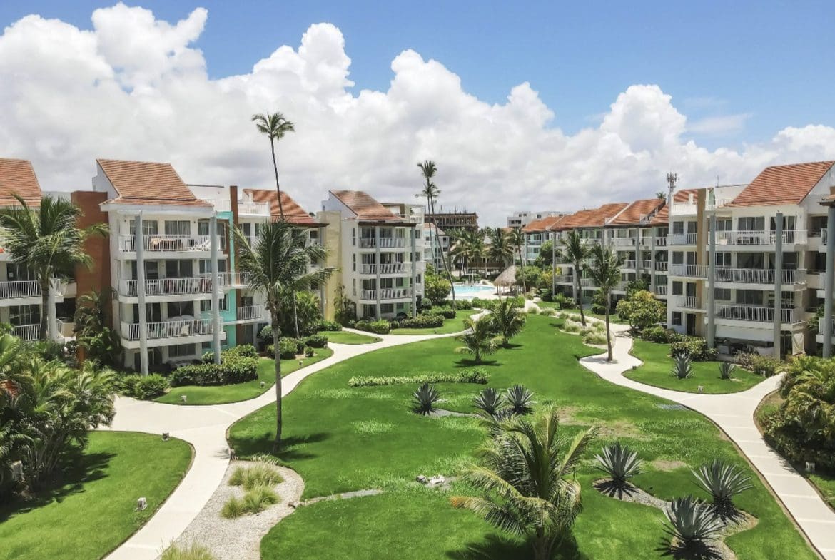 buyDRproperty Tropical resort with condos, lush green lawn, palm trees, and a swimming pool under a blue sky. Sosua Real Estate