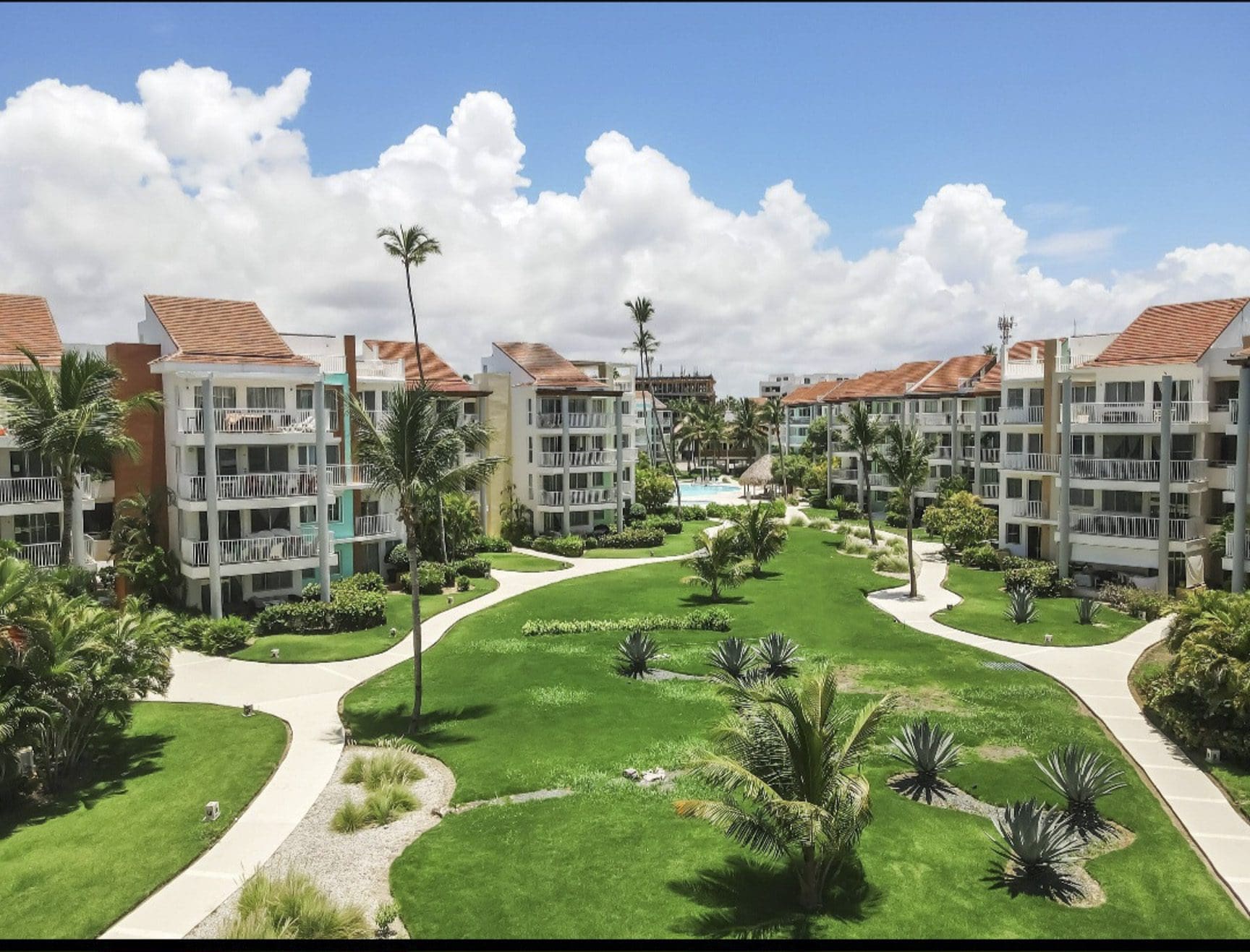 buyDRproperty Tropical resort with condos, lush green lawn, palm trees, and a swimming pool under a blue sky. Sosua Real Estate