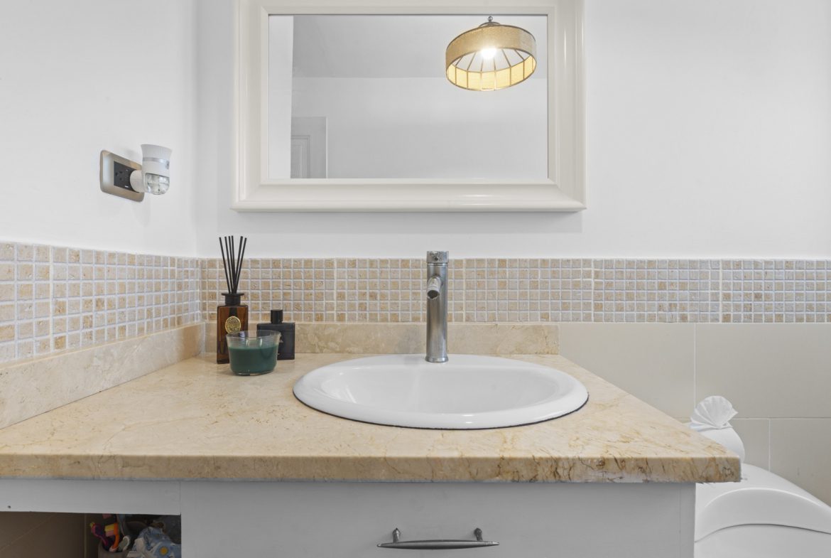 buyDRproperty Bathroom vanity with a white sink, beige countertop, and decorative mirror. Sosua Real Estate