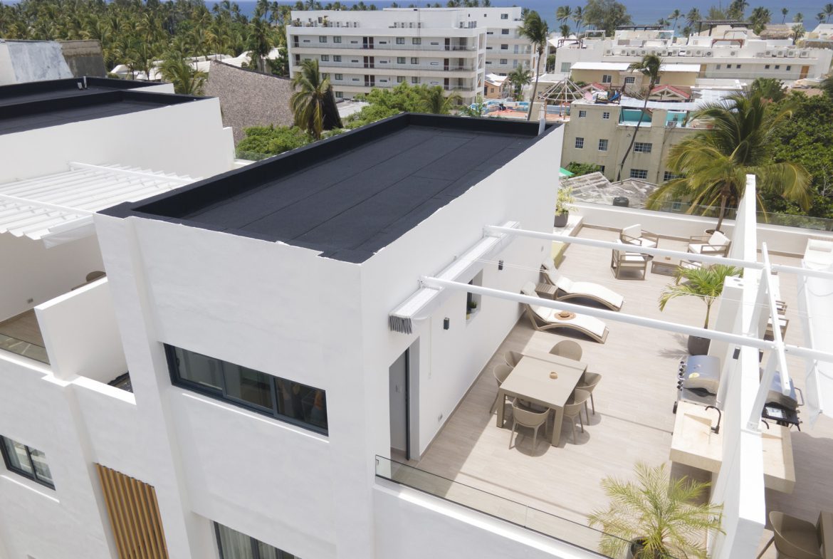 buyDRproperty Rooftop patio with modern furniture, palm trees, and ocean view in a tropical setting. Sosua Real Estate