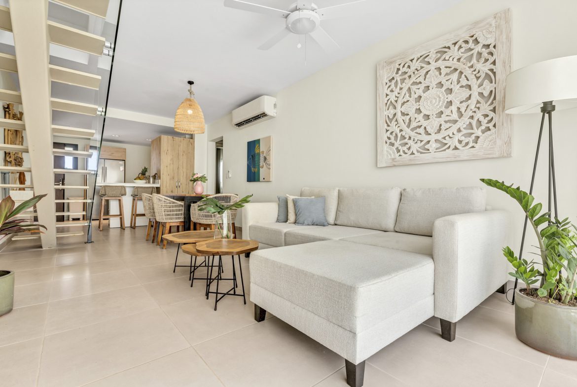 buyDRproperty Bright living room with white sofa, wooden coffee tables, and open staircase, creating a modern, airy space. Sosua Real Estate