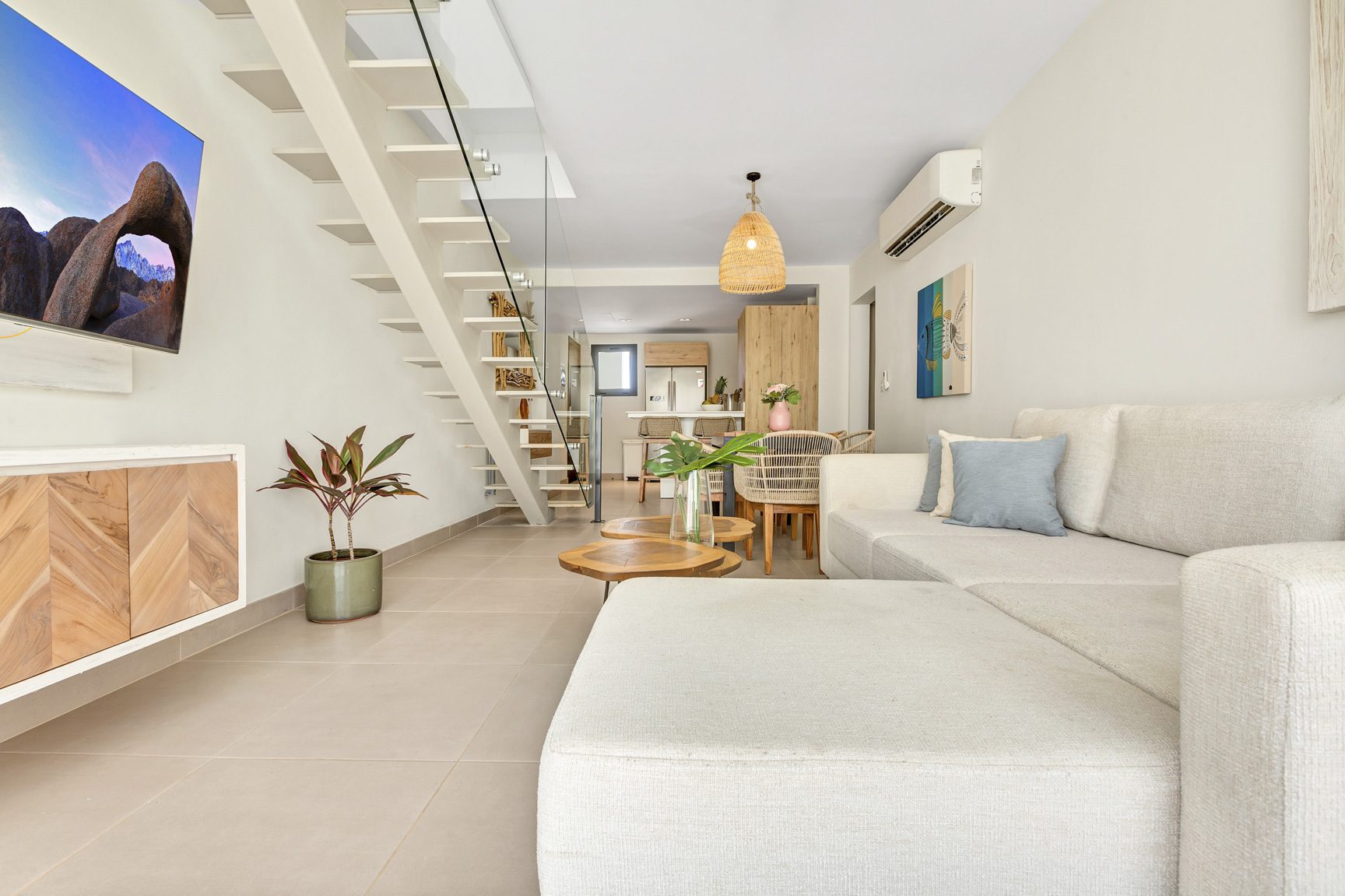 buyDRproperty Bright, modern living room with white sofa, wooden coffee tables, and staircase leading upstairs. Sosua Real Estate