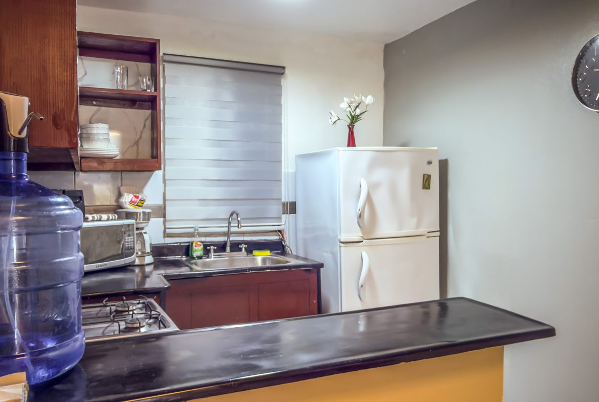 buyDRproperty Compact kitchen with white refrigerator, dark countertops, and wooden cabinets. Sosua Real Estate