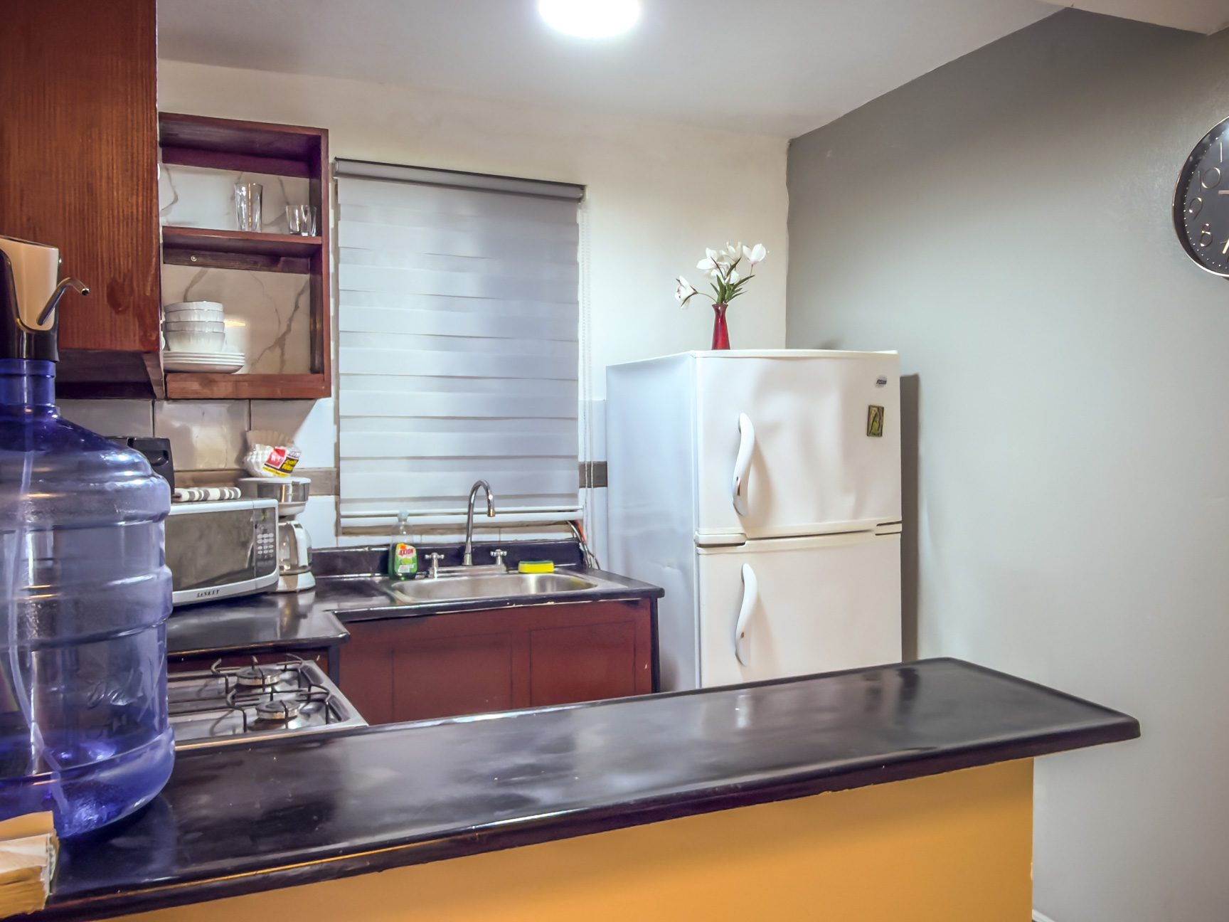 buyDRproperty Compact kitchen with white refrigerator, dark countertops, and wooden cabinets. Sosua Real Estate