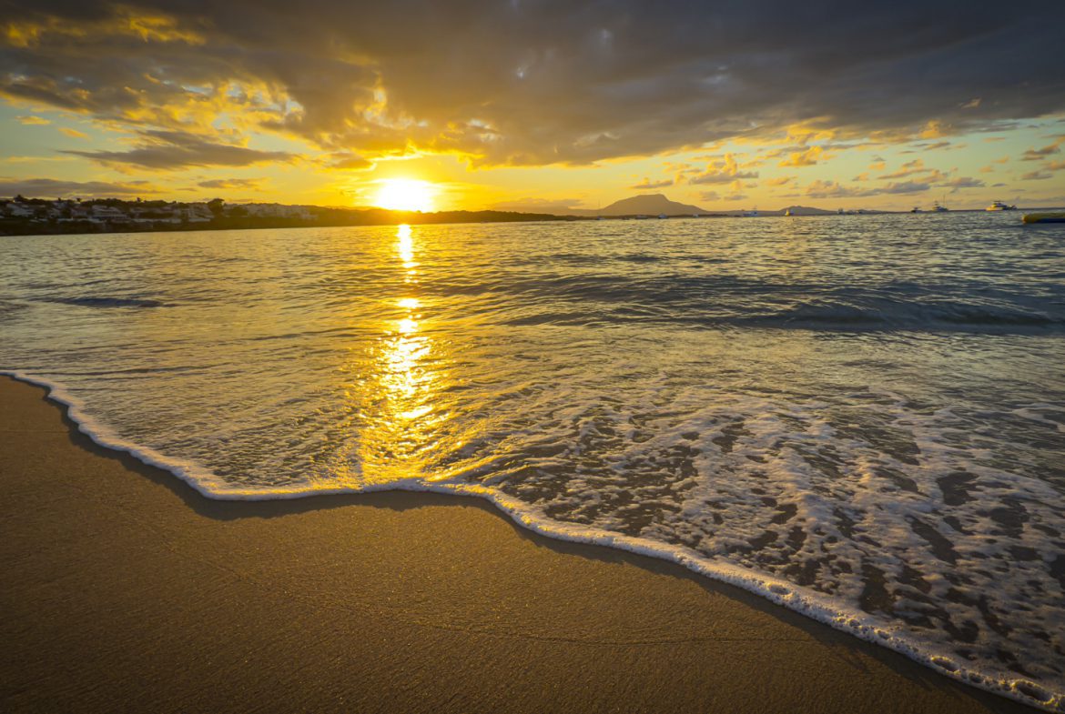 buyDRproperty Golden sunset reflecting on a tranquil beach with gentle waves and distant boats. Sosua Real Estate