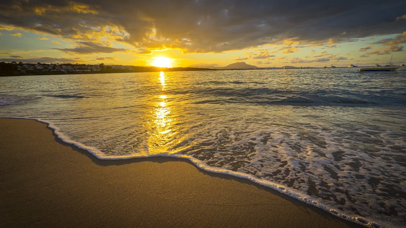 buyDRproperty Golden sunset reflecting on a tranquil beach with gentle waves and distant boats. Sosua Real Estate