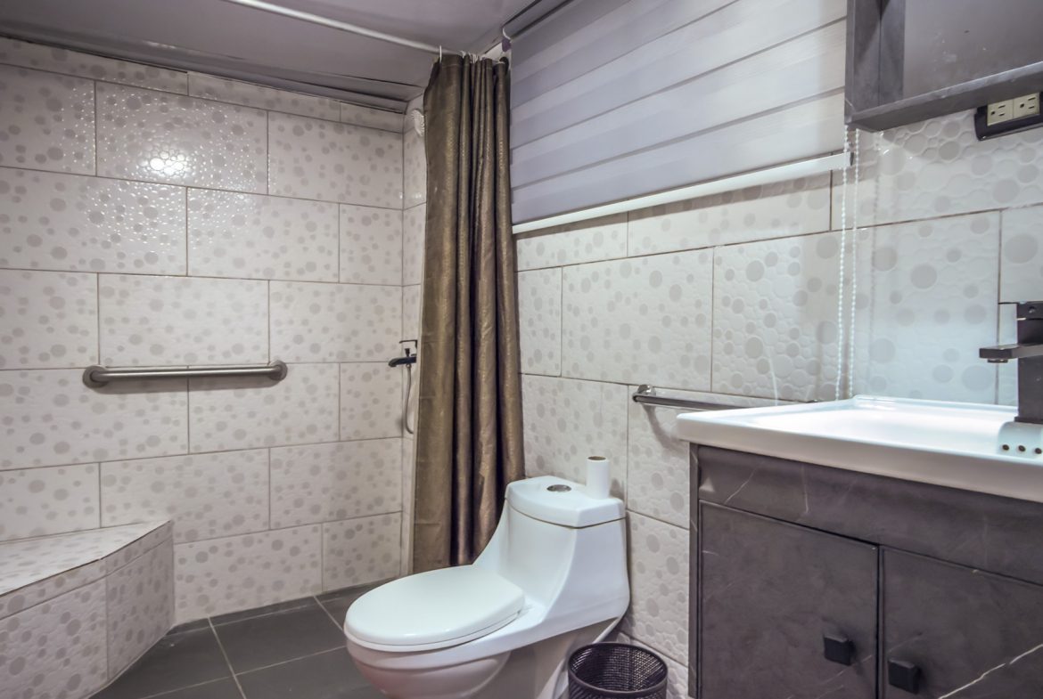 buyDRproperty Accessible bathroom with shower, grab bar, toilet, and sink vanity with grey cabinets. Sosua Real Estate