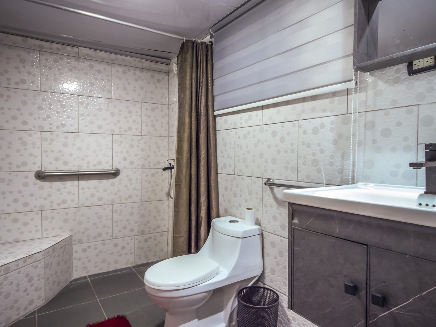 buyDRproperty Accessible bathroom with shower, grab bar, toilet, and sink vanity with grey cabinets. Sosua Real Estate