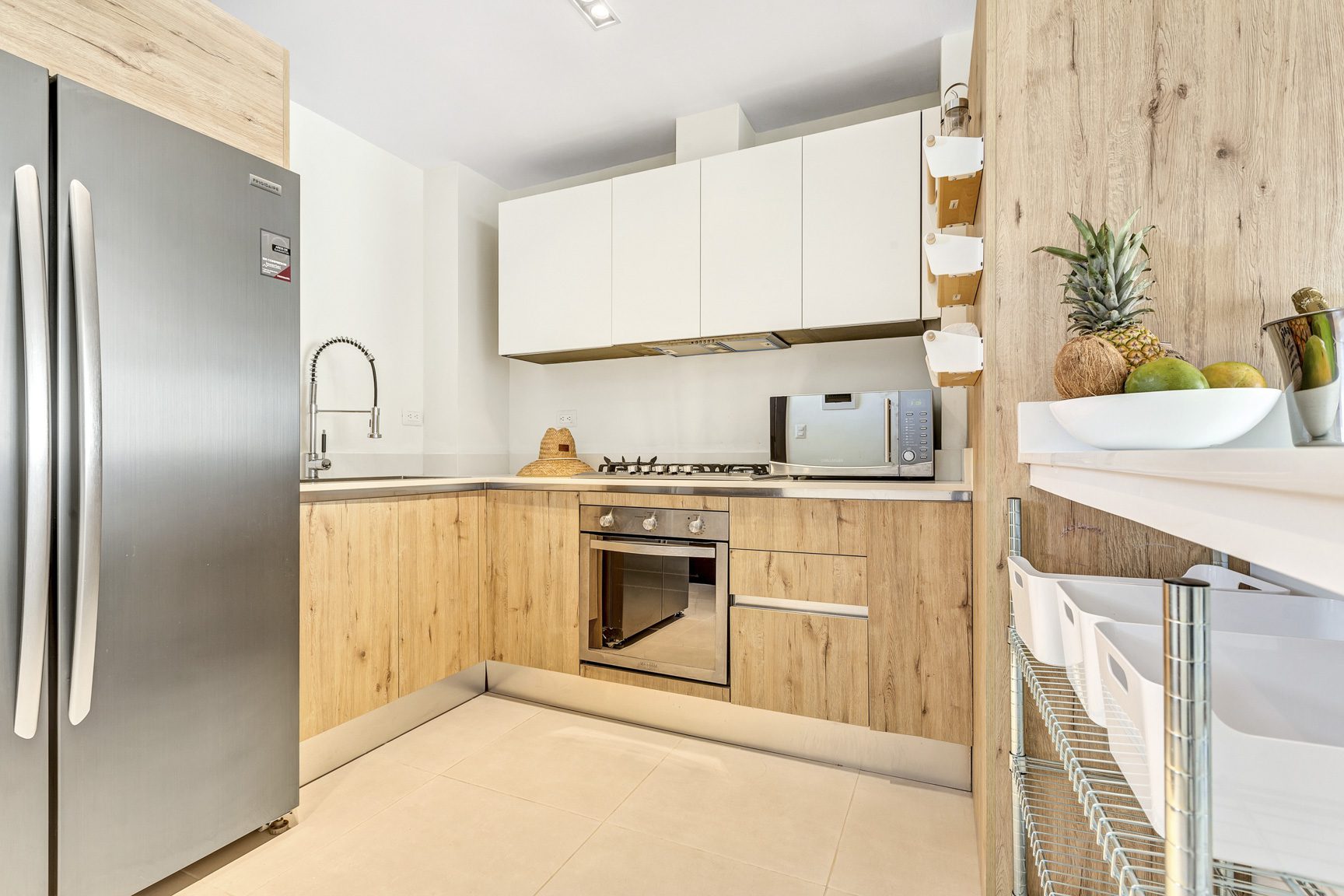 buyDRproperty Modern kitchen with stainless steel appliances, wood cabinets, and tropical fruit display. Sosua Real Estate