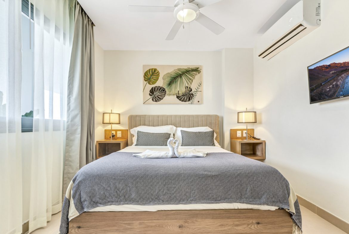 buyDRproperty Bedroom with bed, swan pillows, bedside lamps, and tropical art Sosua Real Estate