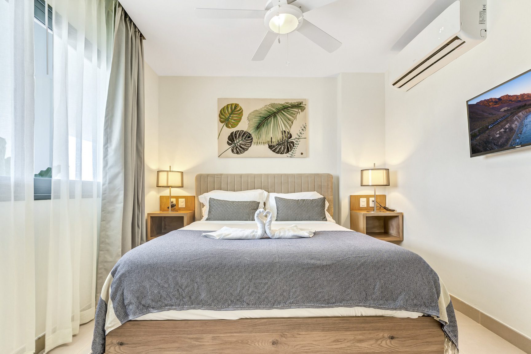buyDRproperty Bedroom with bed, swan pillows, bedside lamps, and tropical art Sosua Real Estate