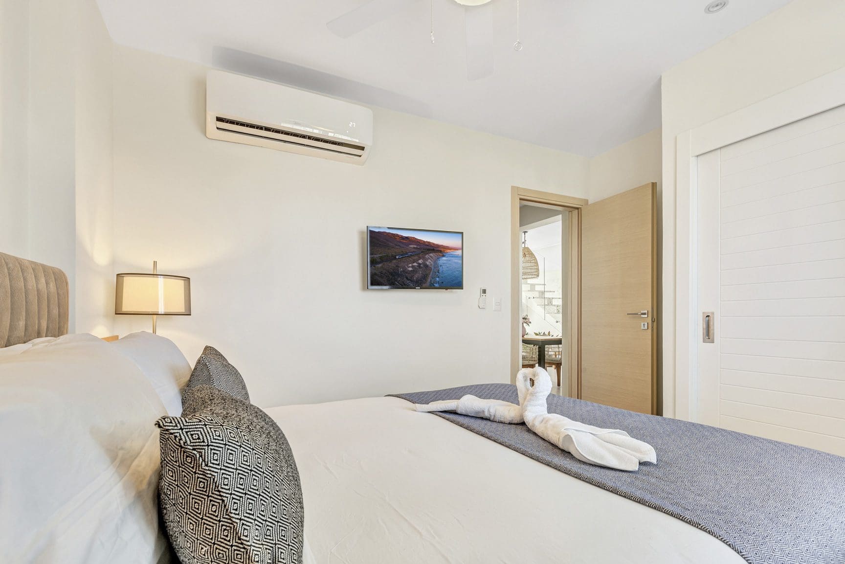 buyDRproperty Modern bedroom with swan towel art on bed, TV, and air conditioner. Clean, bright interior design. Sosua Real Estate