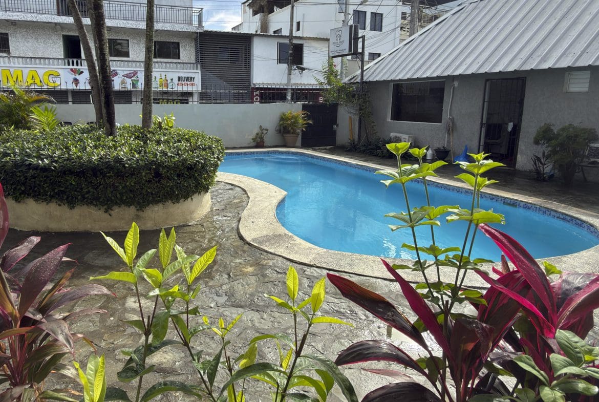 buyDRproperty Bright blue swimming pool surrounded by lush tropical plants and buildings. Sosua Real Estate