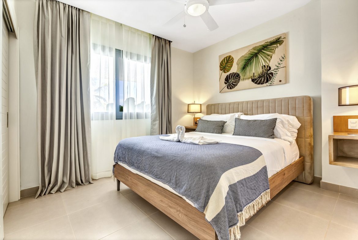 buyDRproperty Bright bedroom with queen bed, linen curtains, tropical art, and gray and white blanket. Sosua Real Estate