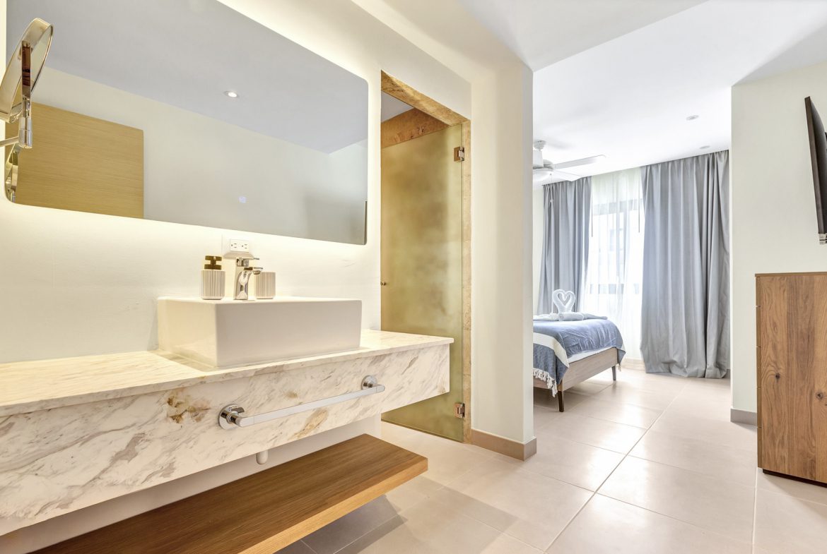 buyDRproperty Modern bathroom with marble vanity and view into bedroom with blue bedding. Sosua Real Estate