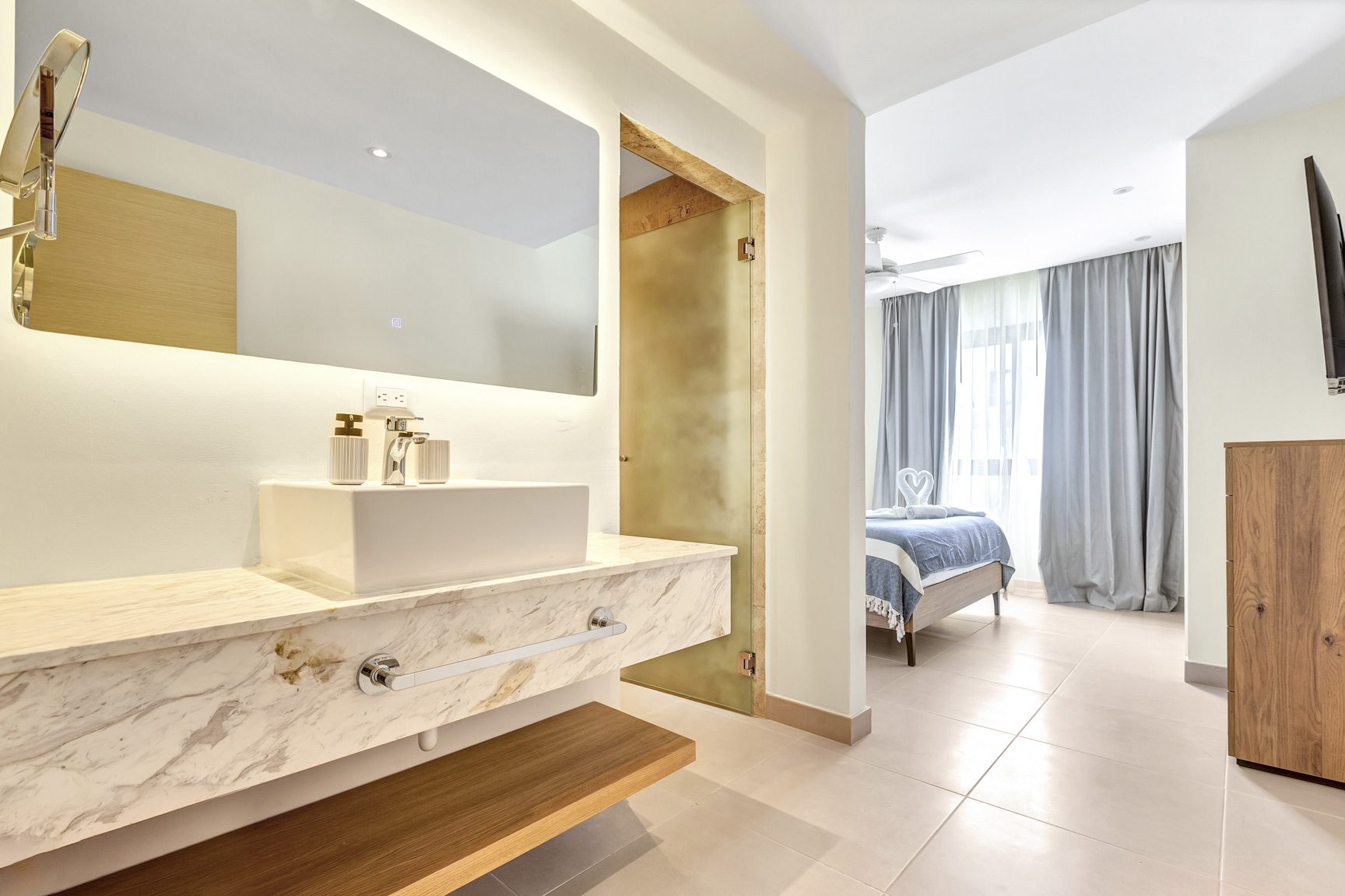 buyDRproperty Modern bathroom with marble vanity and view into bedroom with blue bedding. Sosua Real Estate