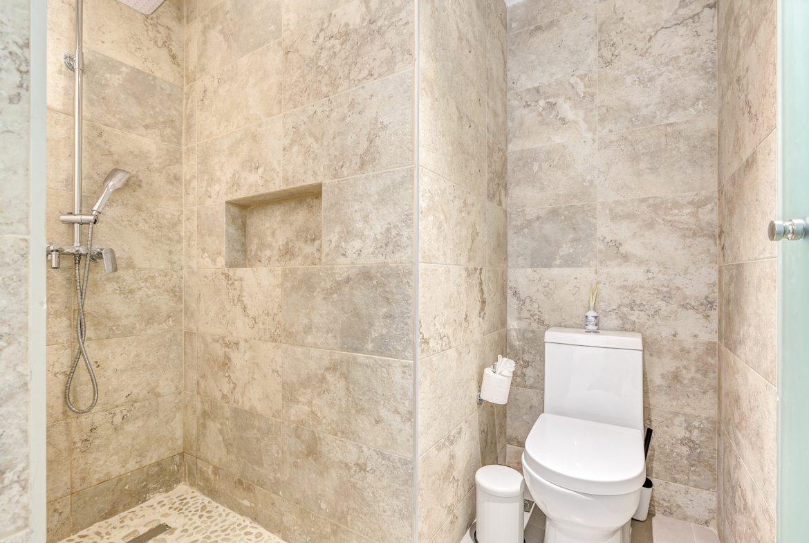 buyDRproperty Modern bathroom with tiled shower, built-in niche, toilet, and stone-look walls. Sosua Real Estate