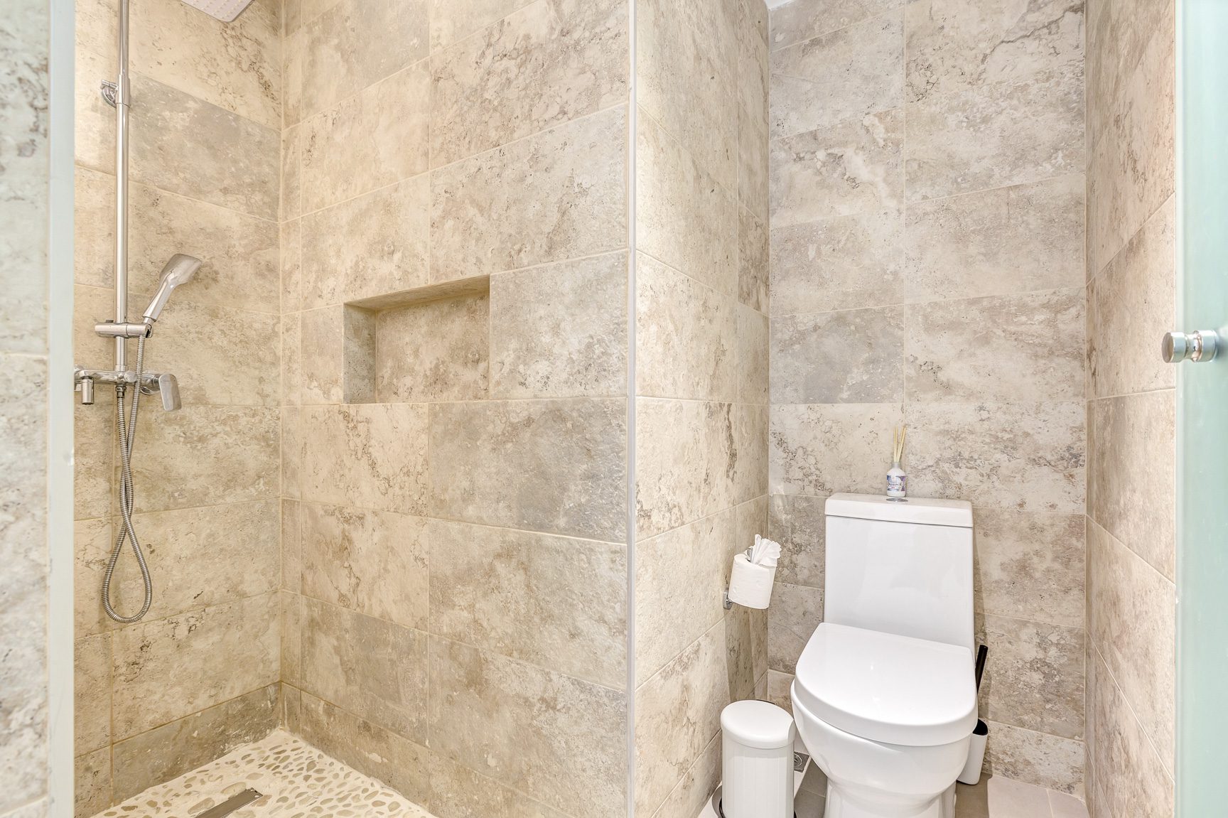 buyDRproperty Modern bathroom with tiled shower, built-in niche, toilet, and stone-look walls. Sosua Real Estate