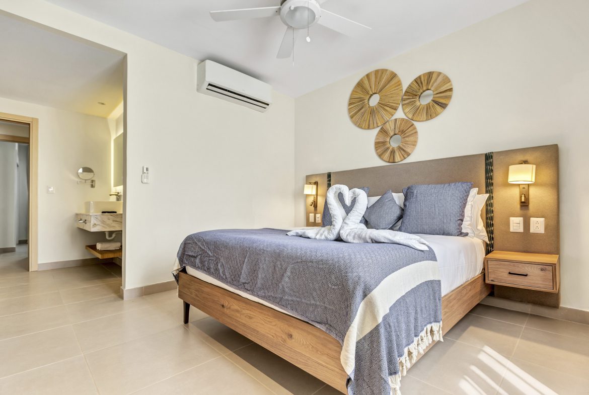 buyDRproperty Hotel bedroom with king-size bed, swan towel art, and modern bathroom entrance. Sosua Real Estate