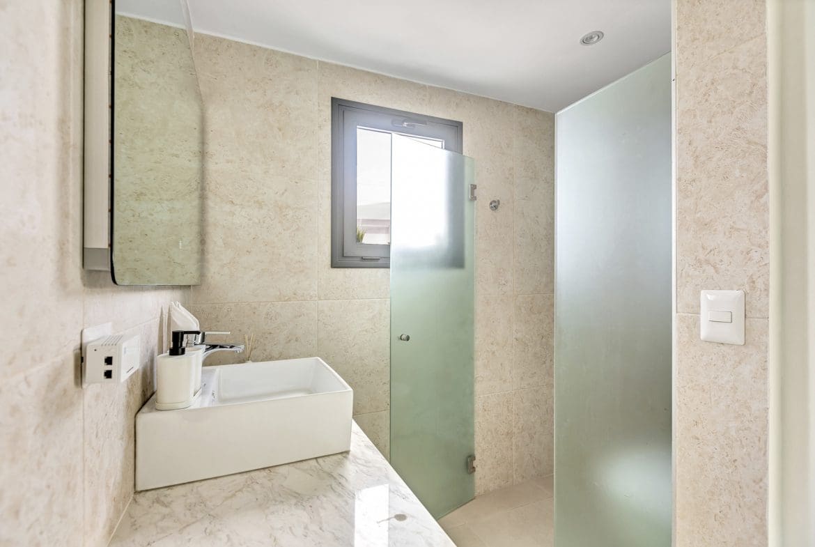 buyDRproperty Modern bathroom with square sink, marble countertop, frosted glass shower, and small window. Sosua Real Estate