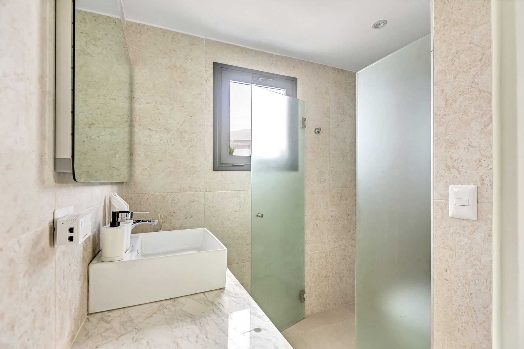 buyDRproperty Modern bathroom with square sink, marble countertop, frosted glass shower, and small window. Sosua Real Estate