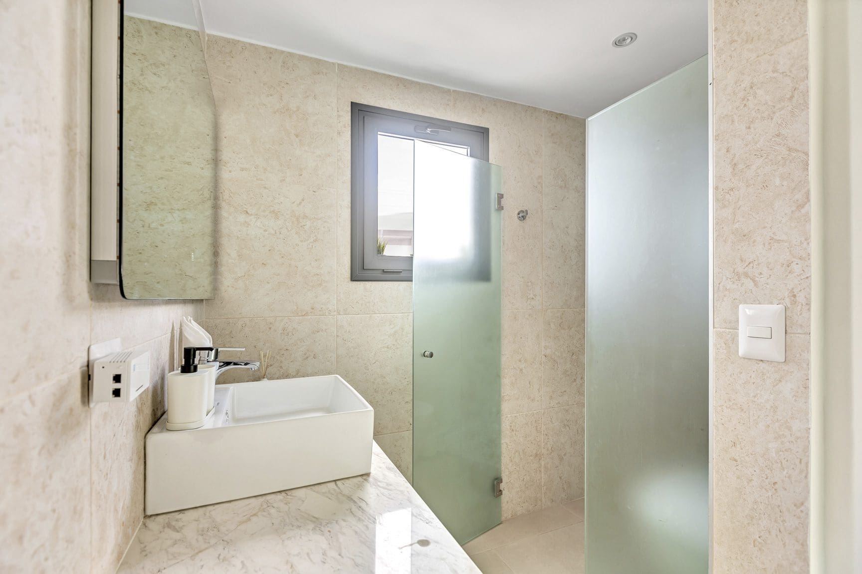 buyDRproperty Modern bathroom with square sink, marble countertop, frosted glass shower, and small window. Sosua Real Estate