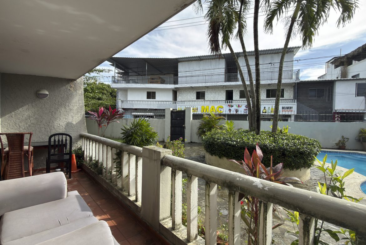buyDRproperty Balcony view of a building with "MAC Delivery" sign, palm trees, and a pool in a tropical location. Sosua Real Estate
