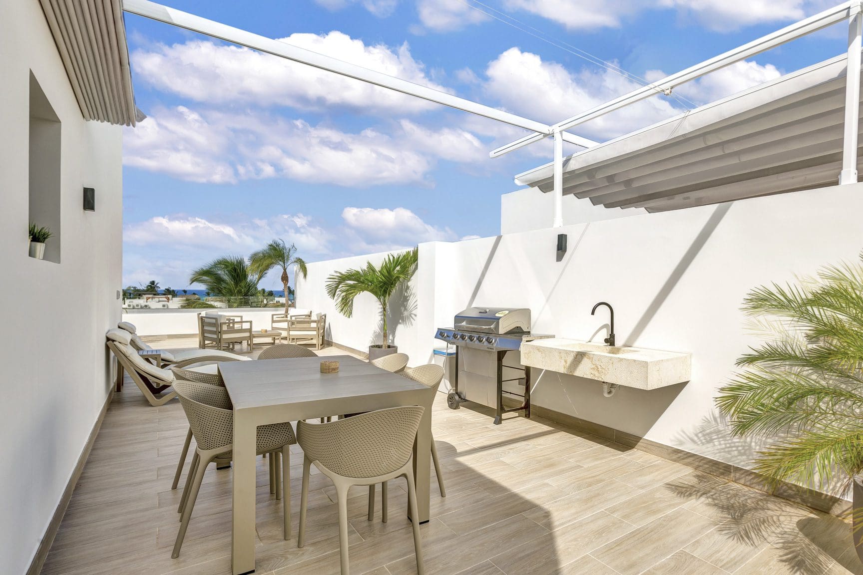 buyDRproperty Outdoor patio with dining table, grill, sink, lounge chairs, palm trees, and a blue sky with clouds. Sosua Real Estate