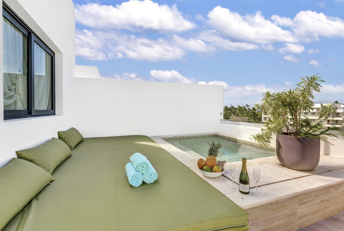 buyDRproperty Rooftop terrace with plunge pool, daybed, towels, fruit, and champagne against a blue sky. Sosua Real Estate