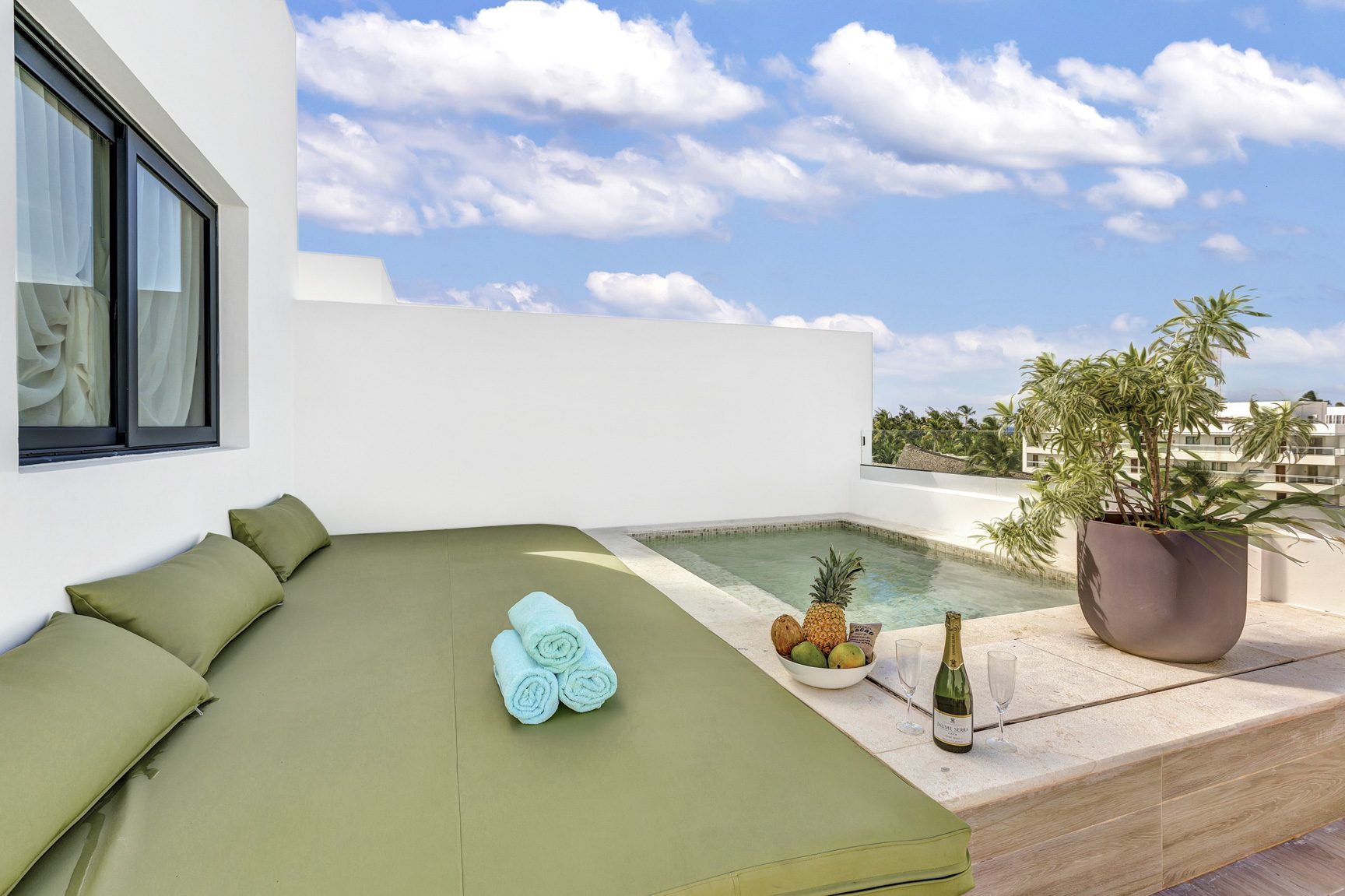 buyDRproperty Rooftop terrace with plunge pool, daybed, towels, fruit, and champagne against a blue sky. Sosua Real Estate