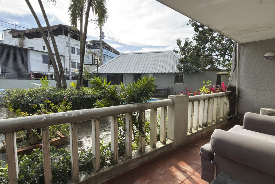 buyDRproperty Balcony view from a Cabarete vacation rental, showcasing tropical plants and nearby buildings. Sosua Real Estate