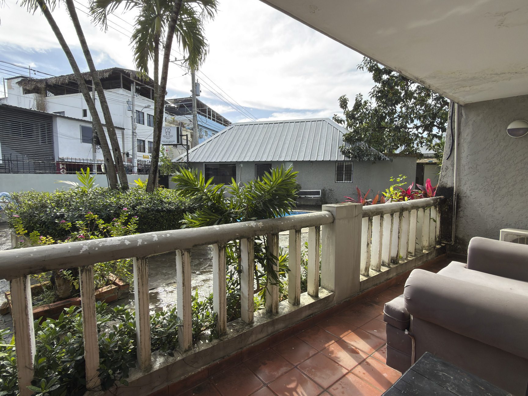 buyDRproperty Balcony view from a Cabarete vacation rental, showcasing tropical plants and nearby buildings. Sosua Real Estate