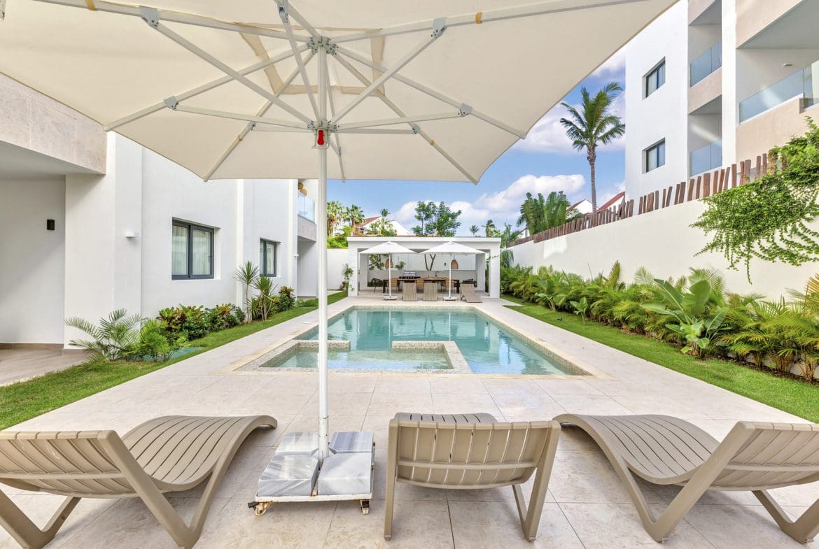 buyDRproperty Luxury pool area with lounge chairs, umbrella, and modern architecture. Tropical resort vibes. Sosua Real Estate