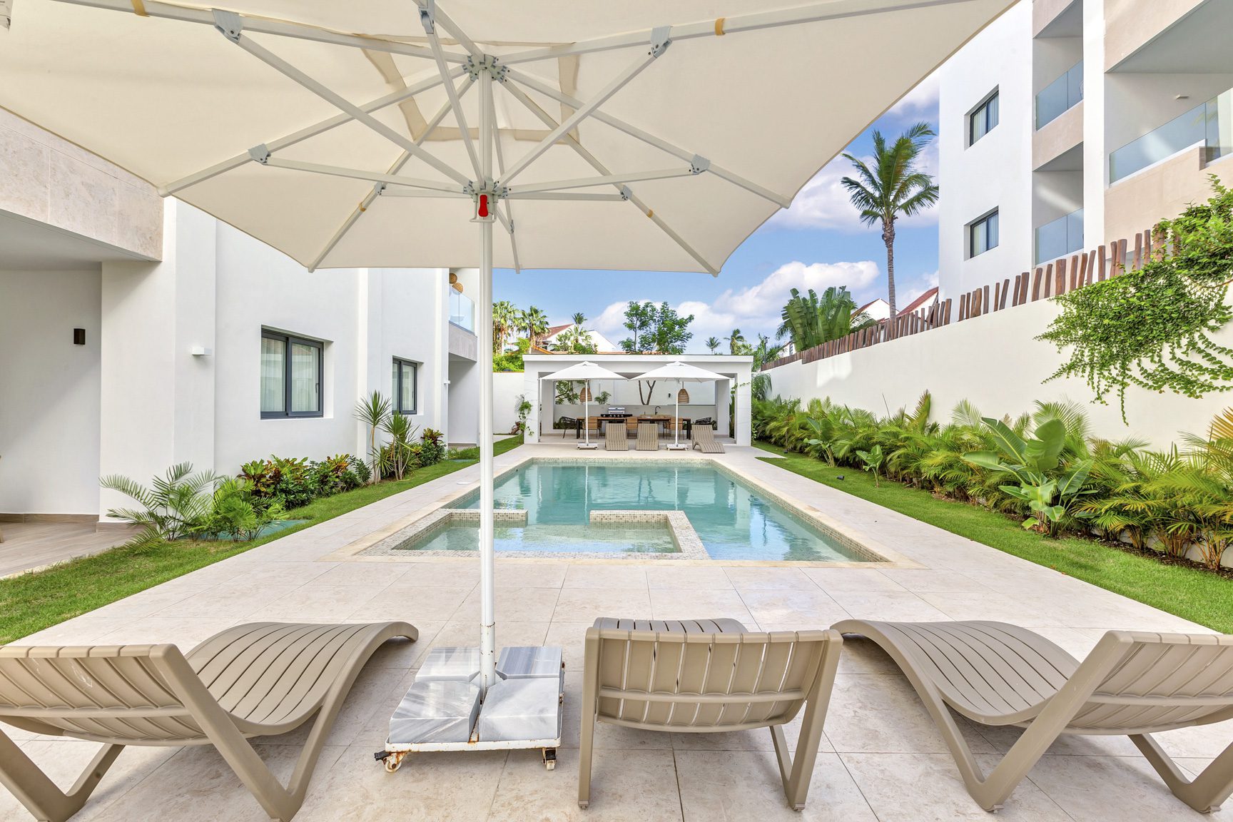 buyDRproperty Luxury pool area with lounge chairs, umbrella, and modern architecture. Tropical resort vibes. Sosua Real Estate
