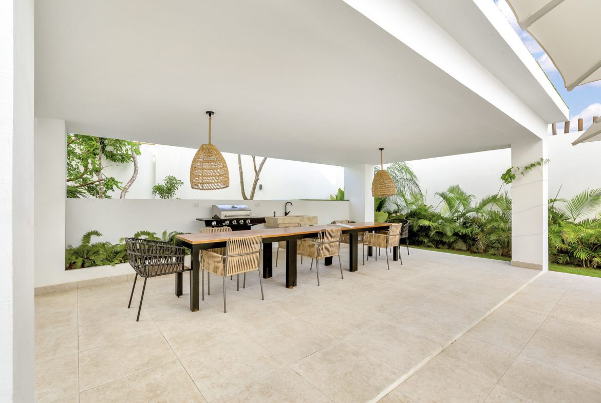buyDRproperty Covered outdoor dining area with long table, chairs, grill, and lush greenery. Sosua Real Estate