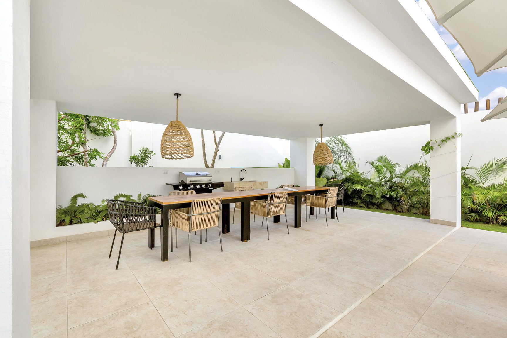 buyDRproperty Covered outdoor dining area with long table, chairs, grill, and lush greenery. Sosua Real Estate