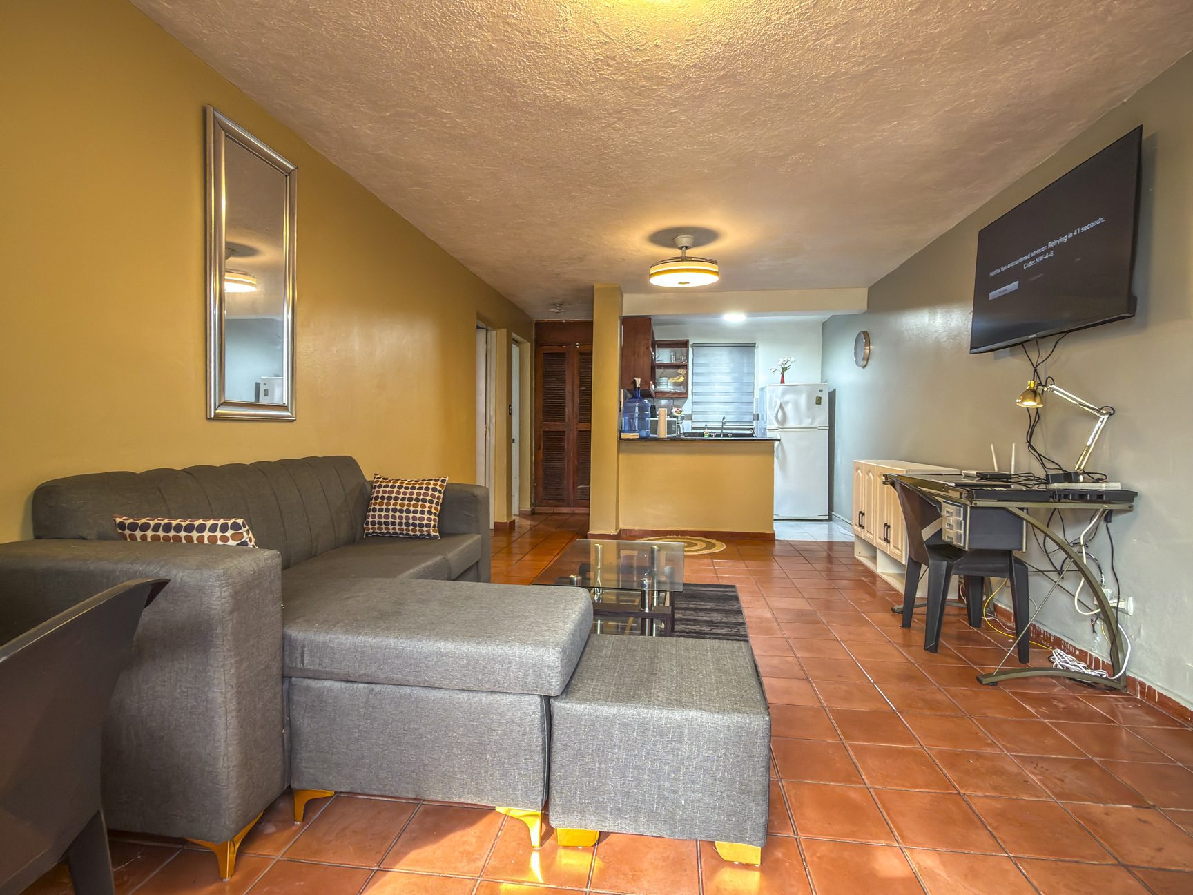 buyDRproperty Cozy living room with gray sectional sofa, terracotta tile floor, and open kitchen in background. Sosua Real Estate